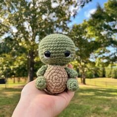 a small crocheted turtle sitting on top of a person's hand in the grass