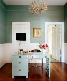 a white desk sitting in the middle of a living room next to a lamp and door