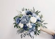 a bridal bouquet with blue and white flowers is being held by someone's hand