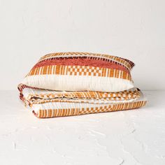 two pillows sitting on top of each other in front of a white wall and floor