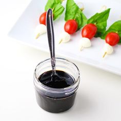 a jar filled with black liquid next to small tomatoes on a white plate and green leaves