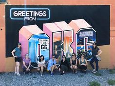 a group of people are posing in front of a wall with the words greetings from kl painted on it