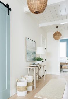 a hallway with white walls and wooden floors, two baskets on the floor next to a table