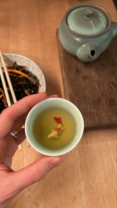 a person holding a small bowl of green tea with chopsticks in front of them