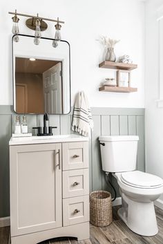 a white toilet sitting under a bathroom mirror next to a wooden shelf filled with towels