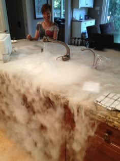 a woman standing in front of a kitchen counter covered in steam from a faucet