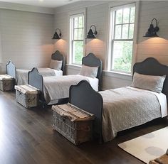 two twin beds in a room with wooden floors and white walls, along with three windows