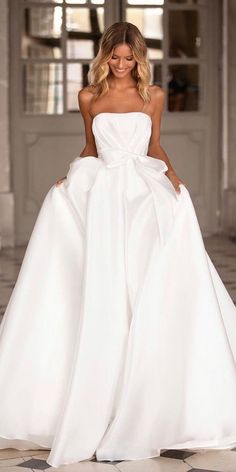 a woman in a white wedding dress standing on a tiled floor with her hands on her hips