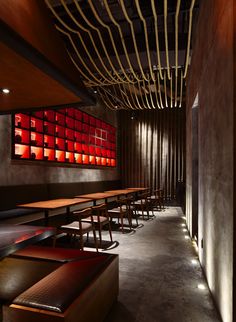 an empty restaurant with wooden benches and red lights on the wall behind them, along with long tables