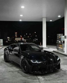 a black sports car parked in front of a gas station at night with its lights on