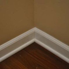 the corner of a room with wood flooring and white trim on the wall above it