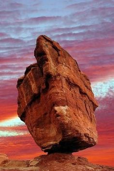 a large rock sitting on top of a rocky hill under a colorful sky with clouds