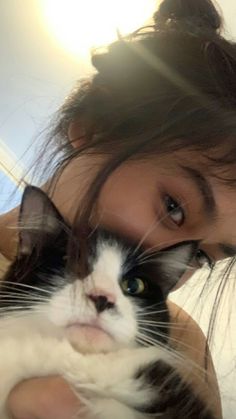 a woman holding a black and white cat in her arms while looking at the camera