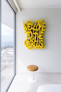 a yellow sign that says welcome to the circus on a white wall next to a bench