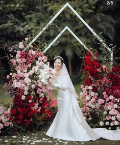 a woman in a wedding dress standing next to flowers and an arch with roses on it