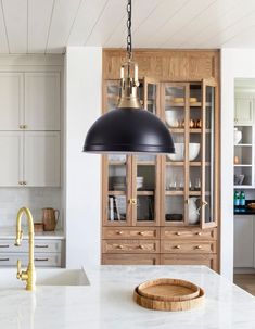 a kitchen with white counter tops and wooden cabinets in the background, along with a large black pendant light hanging from the ceiling