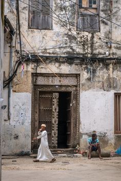 two people sitting on the ground in front of an old building with wires above them