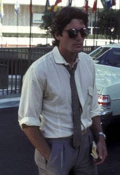 a man wearing sunglasses and a tie standing in front of a car