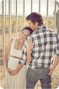 a man and woman standing next to each other in front of a fence with their backs turned