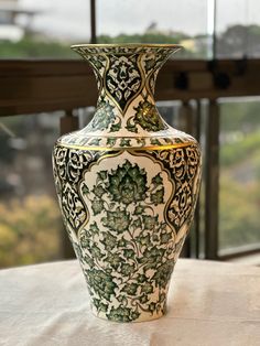 a green and white vase sitting on top of a table next to a large window