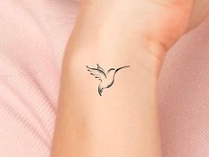 a small black bird tattoo on the left inner arm and wrist is shown in front of a woman's pink shirt