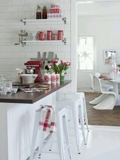 a white kitchen with red accents and pink flowers in vases on the counter top