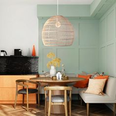 a dining room table and chairs in front of a kitchen with blue walls, wood flooring and an orange pendant light hanging from the ceiling