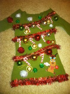 a green sweater with christmas decorations on the top and bottom, is laying on the floor