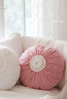 two decorative pillows on a white couch in front of a window with lace trimmings