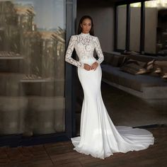 a woman standing in front of a glass door wearing a white dress with long sleeves