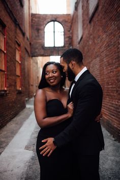 a man and woman standing in an alleyway hugging each other, smiling at the camera