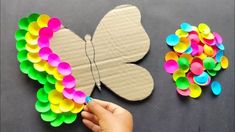 someone is making a butterfly out of paper and colored confetti on the table