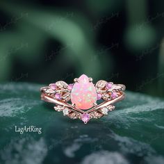 a pink opalite and diamond ring sitting on top of a green leafy surface