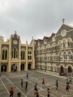 a group of people playing basketball in front of a large building with many arched windows