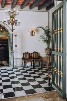 an open door leading into a room with checkered flooring and chandelier