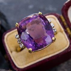 This gorgeous cocktail ring showcases a cushion cut amethyst with a medium-deep hue and lively light return.  The amethyst is accented on each side with three bright diamonds. We love this classic cocktail ring design. The ring is crafted in 14k yellow gold and is currently a size 7. Luxury Cushion Cut Amethyst Ring With Accent Stones, Luxury Diamond Amethyst Ring With Halo Setting, Luxury Large Oval Amethyst Ring, Luxury Gold Round Amethyst Ring, Purple Cushion Ring, Luxury Formal Amethyst Ring, Oval Cabochon, Luxury Unique Amethyst Ring With Accent Stones, Luxury Modern Amethyst Ring With Diamond, Luxury Multi-stone Amethyst Ring