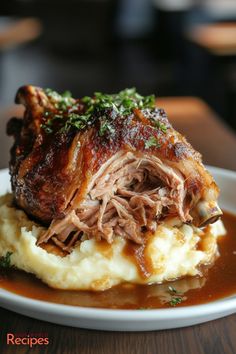 a white plate topped with meat and mashed potatoes on top of a wooden table