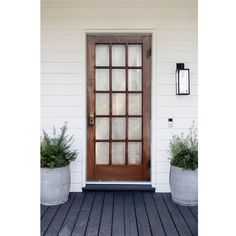 two planters are on the front porch next to a wooden door with glass panes