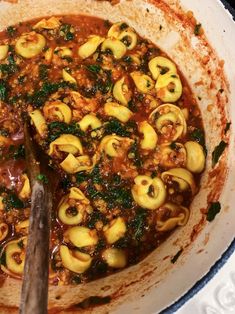 a pot filled with pasta and sauce on top of a stove burner next to a wooden spoon