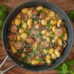 a skillet filled with potatoes and sausages on top of a wooden table next to parsley