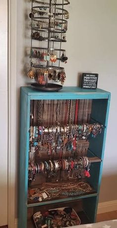 a blue cabinet filled with lots of bracelets and necklaces hanging on it's sides