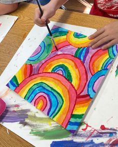 two children are painting rainbows on paper with paintbrushes in front of them