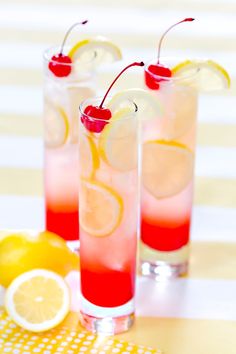 two glasses filled with lemonade and cherries sitting on a table next to sliced lemons