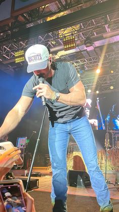 a man holding a microphone on stage with other people in the back ground and lights behind him