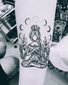 a black and white photo of a person with a tattoo on their arm, sitting in a lotus position