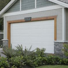 a house with a white garage door in front of it and plants around the driveway