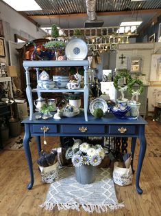 a blue table topped with lots of plates and bowls next to a vase filled with flowers