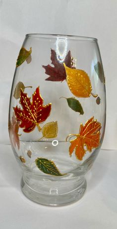 a glass vase with autumn leaves painted on the outside and inside, sitting on a white surface