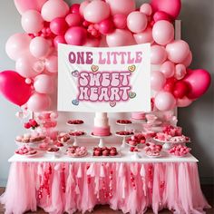 a table topped with lots of pink and white balloons next to a sign that says one little sweet heart