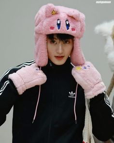 a young person wearing a pink hat and mittens on their head with two stuffed animals in the background